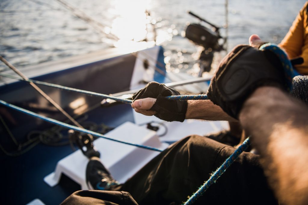 Sailor with gloves pulling on line while mooring yacht